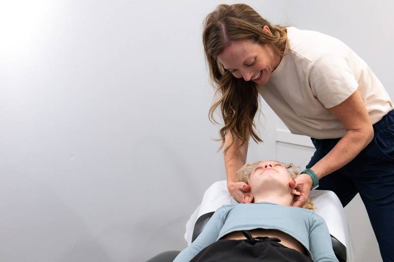 A chiropractor gently supporting a young girl’s neck during treatment