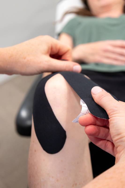 Black kinesiology tape being applied around a patient’s knee